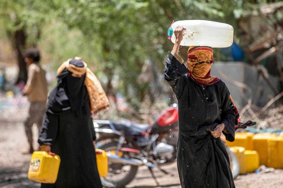 نساء يسرن ويحملن حاويات مملوءة بالمياه من صهريج على مشارف تعز.