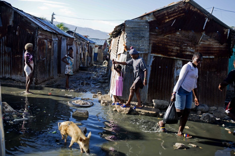 Bewohner*innen und ein kleines Schwein laufen durch Abwasser in einem Viertel im Slum Cite Soleil in Port-au-Prince, Haiti.