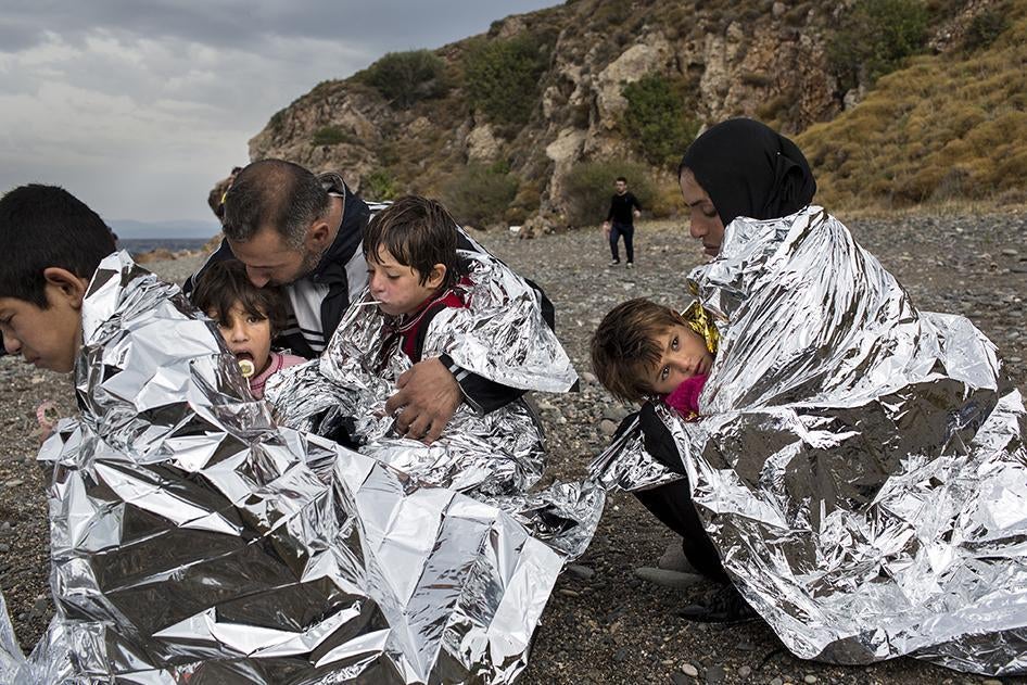 A family sits on the shore of the Greek island of Lesbos wrapped in thermal blankets after journeying from Turkey aboard a rubber boat. October 11, 2015. © 2015 Zalmaï for Human Rights Watch