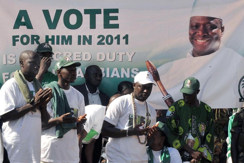 Supporters of Gambian President Yahya Jammeh stand by a campaign poster on November 22, 2011.