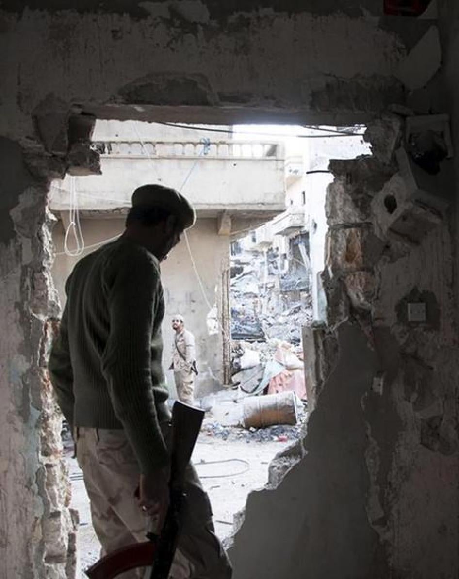 عنصر من الجيش الوطني الليبي، قوات مسلحة متحالفة مع الحكومة الانتقالية في البيضاء، يقف قرب حفرة في جدار أثناء مواجهات مع مجلس شورى ثوار بنغازي، تحالف مكوّن من ميليشيات إسلامية، في بنغازي، ليبيا.
