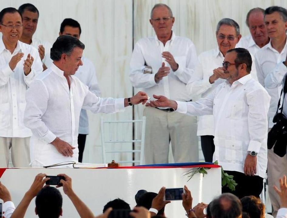Colombian President Juan Manuel Santos hands a lapel pin in shape of a dove to Timochenko after signing a peace accord.