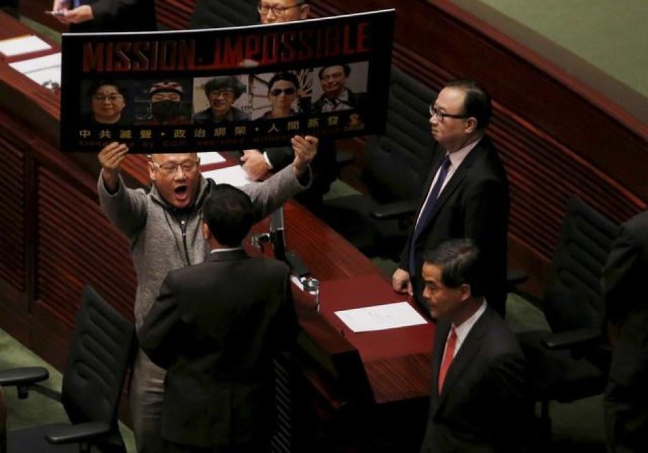泛民议员陈伟业手持五名失踪书商的照片，向刚刚到达立法会议场进行年度施政报告的特首梁振英大声抗议，中国香港，2016年1月13日。