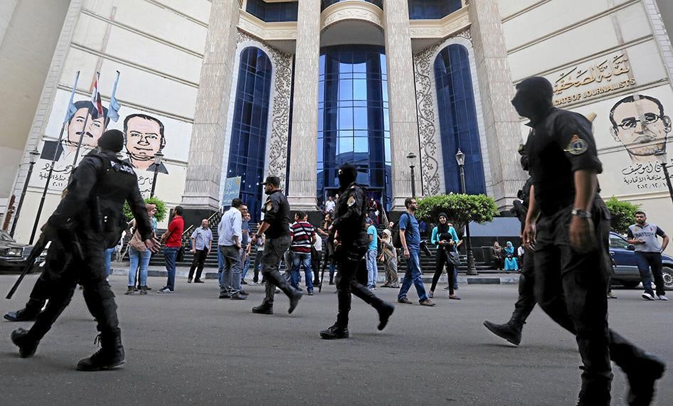 Masked Egyptian security forces walk by a demonstration held by journalists and activists against the detention of journalists, in front of the Press Syndicate in Cairo, Egypt on April 26, 2016.