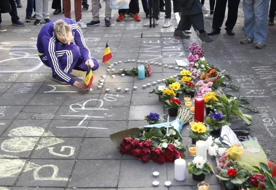 Un homme dépose un drapeau belge près de bouquets de fleurs et de bougies, en hommage aux victimes des attaques à la bombe commises à Bruxelles, le 22 mars 2016.