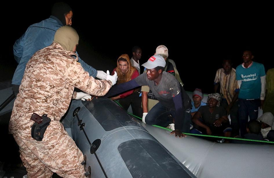 عنصر في حرس السواحل الليبي يساعد مهاجرين على الصعود إلى مركب للبحرية الليبية متجه إلى طرابلس، بعد أن تم اعتراض المهاجرين واحتجازهم في 20 سبتمبر/أيلول 2015. 
