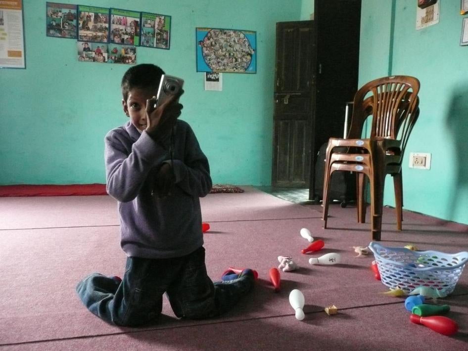 A young boy sitting on the floor of a daycare center, playing with a camera. Suraj, a 9-year-old boy with a physical disability, does not attend school because his parents thought that no school would admit him. He recently started attending a nearby dayc
