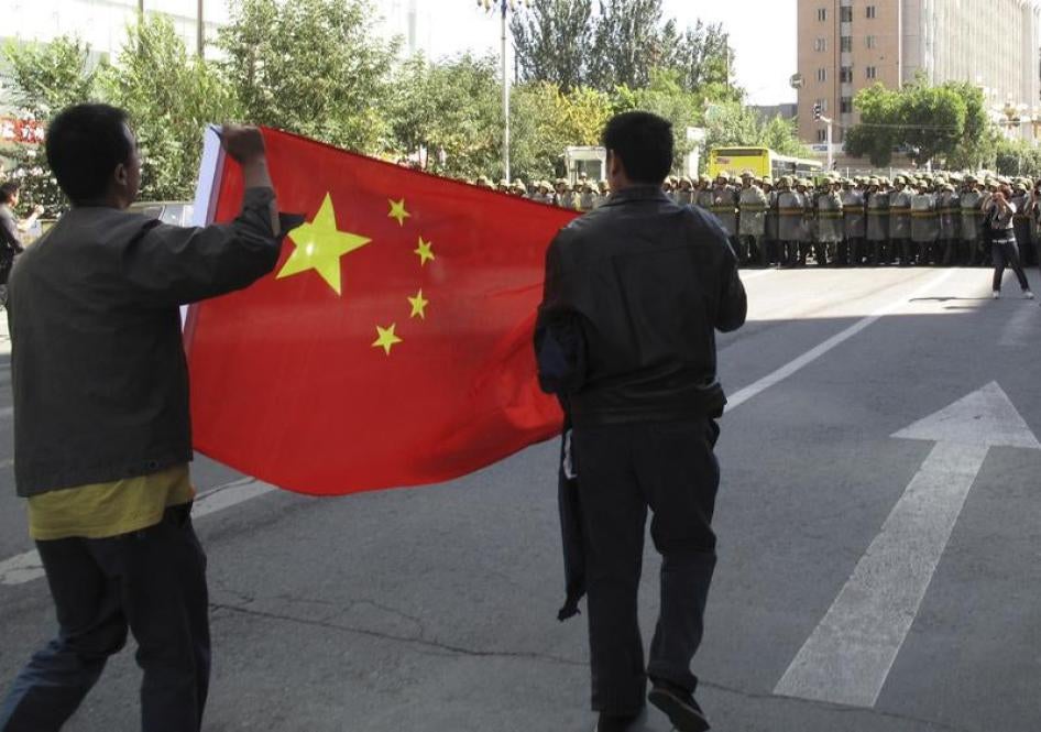 Han Chinese residents hold a Chinese national flag as paramilitary policemen in riot gear block a road at the centre of Urumqi in China's Xinjiang Autonomous Region September 3, 2009.