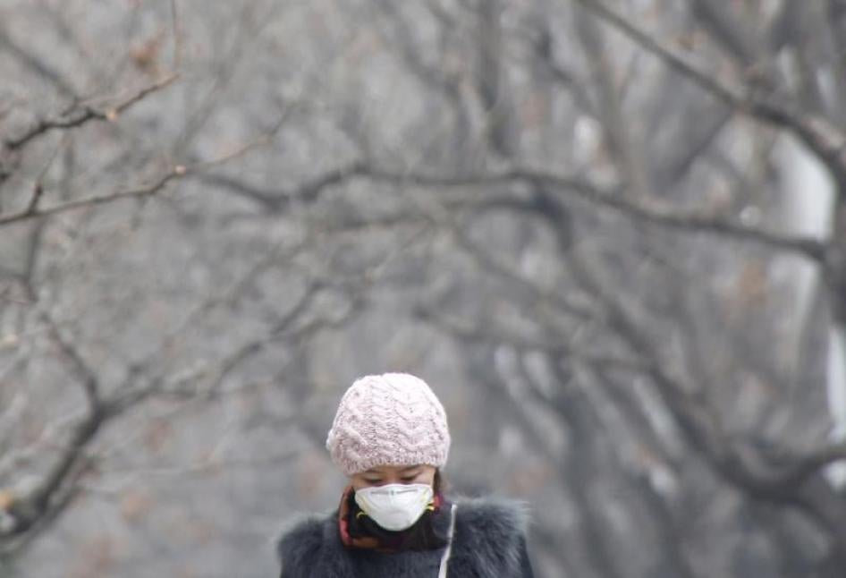 一名女性戴着口罩走在北京空气污染严重的北京街道，2015年12月26日。