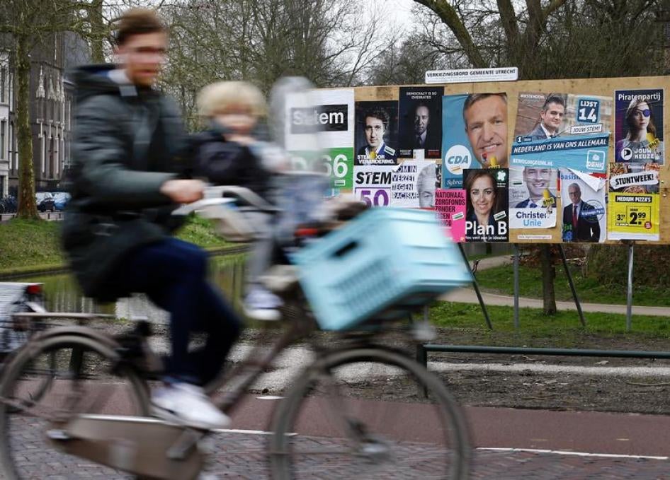 Een man fietst met een kind langs een billboard met verkiezingsposters, een dag voor de Tweede Kamerverkiezingen, in Utrecht, Nederland, 14 maart 2017.
