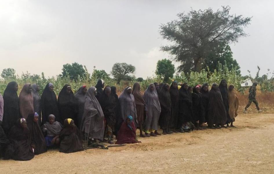 A man carrying a Boko Haram flag walks past a group of 82 Chibok girls, who were held captive for three years by Islamist militants, as the girls wait to be released in exchange for several militant commanders, near Kumshe, Nigeria May 6, 2017.
