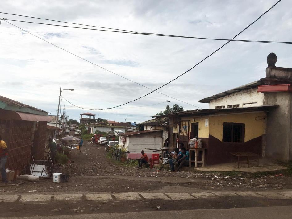 A wide shot of houses in a neighborhood of Malabo, Equatorial Guinea, with unpaved roads, one-storey houses, and trash 