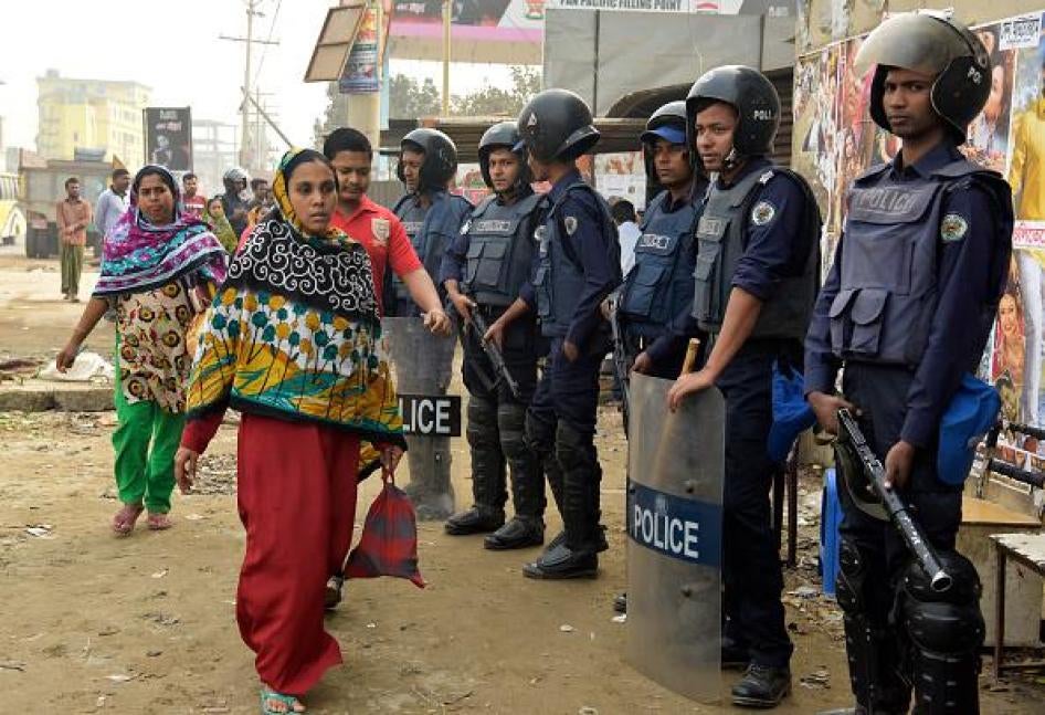 Des employées et employés d’une usine de confection à Ashulia, une banlieue de Dhaka, la capitale du Bangladesh, passent devant une rangée de policiers anti-émeute le 26 décembre 2016, date de la recouverte de plusieurs usines après cinq jours de fermetur