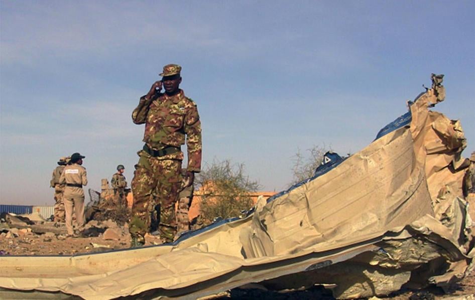 A soldier surveys the debris following a November 29, 2016 suicide car bomb attack at the Gao airport, used primarily by UN forces stationed there. The attack was claimed by the armed group Al-Mourabitoun, whose forces committed the war crime of perfidy b