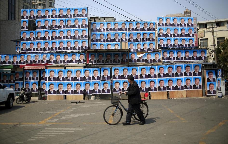A man with a bicycle walks past a building covered in posters of Chinese President Xi Jinping in Shanghai, March 26, 2016. 