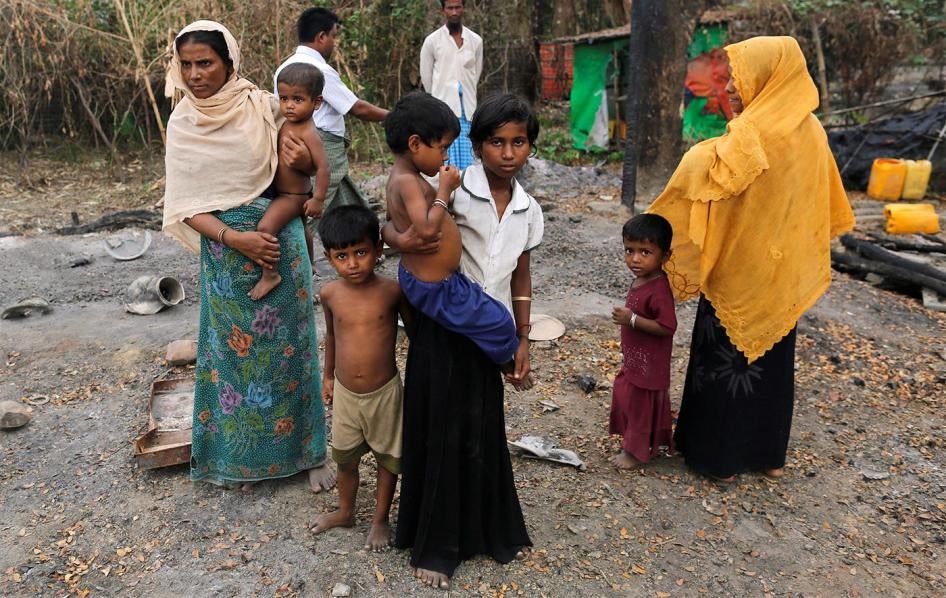 A family stands beside the remains of a burned down market in a Rohingya village outside Maungdaw, Rakhine State on October 27, 2016.