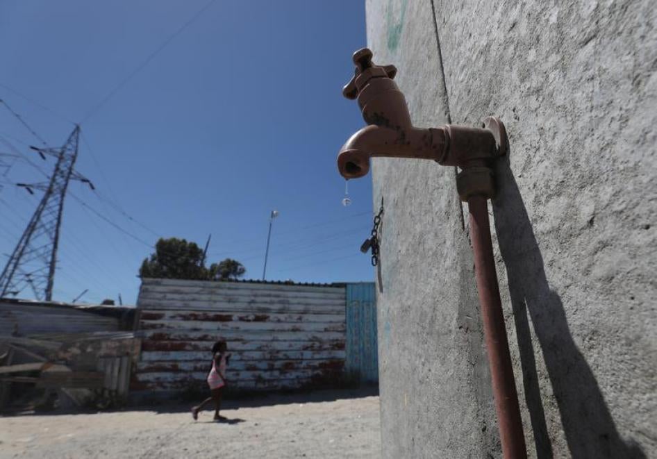 Residents walk past a leaking communal tap in Khayelitsha township, near Cape Town, South Africa, December 12, 2017.