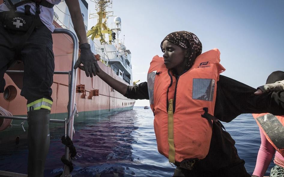 Des secouristes de SOS MEDITERRANEE aident une Somalienne à se hisser de leur bateau gonflable à coque rigide (RHIB) sur l'Aquarius.