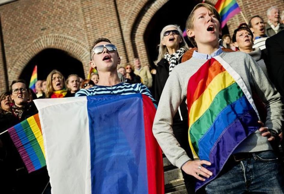 People sing the Russian national anthem while raising rainbow flags and a Russian flag in solidarity with the lesbian, gay, bisexual and transgender (LGBT) community of Russia