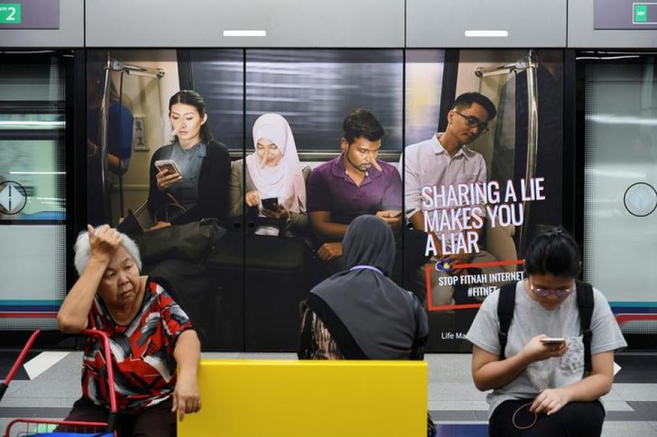 Commuters sit in front of an advertisement discouraging the dissemination of fake news, at a train station in Kuala Lumpur, Malaysia March 28, 2018.