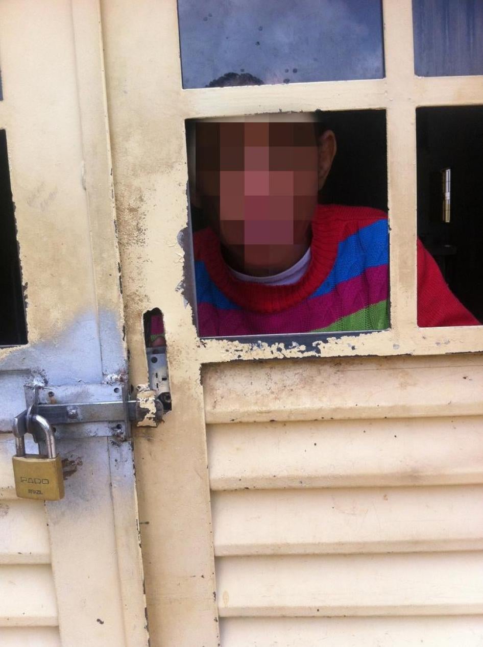Um homem com deficiência intelectual, vivendo em uma instituição para 51 pessoas com deficiência nos arredores de Brasília, Distrito Federal, espia através de uma porta trancada.