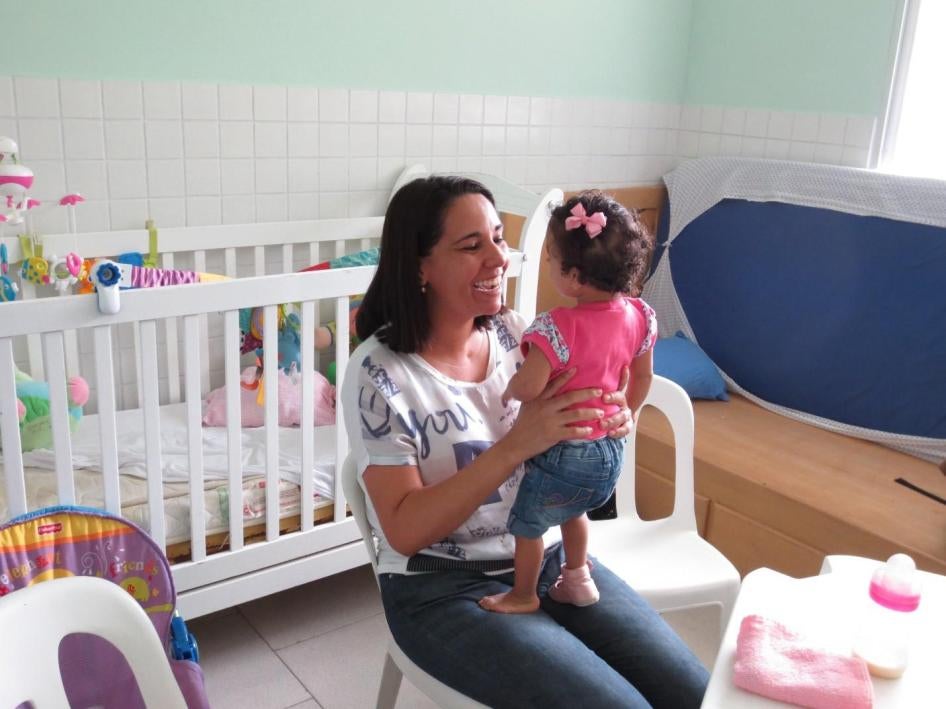 Uma mãe com sua filha adotiva de 3 anos que tem deficiência de desenvolvimento. O governo brasileiro deve expandir programas de adoção e acolhimento familiar para assegurar que crianças com deficiência cresçam em famílias, e não em instituições. 