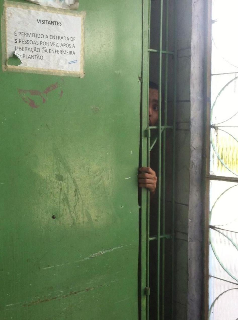 Um homem com deficiência espia pelas grades da ala psiquiátrica de uma instituição no Rio de Janeiro. Pessoas confinadas nesta área da instituição nunca deixam seus quartos, de acordo com funcionários.