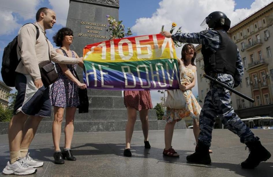 Des personnes participant à un rassemblement de la communauté LGBT à Moscou tiennent un drapeau aux couleurs de l’arc-en-ciel, sur lequel figure le slogan «Faites l’amour, pas la guerre», face à un policier qui s’apprête à intervenir, le 30 mai 2015.