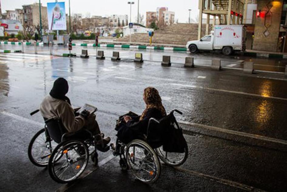 Deux femmes iraniennes en fauteuil roulant, aux abords d’une rue rendue glissante par la pluie, à Téhéran.