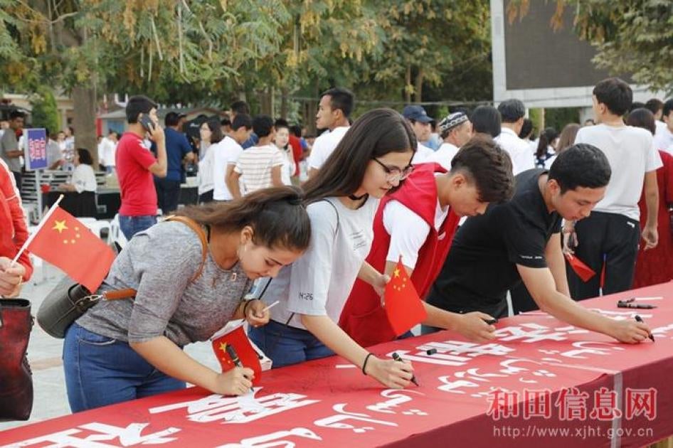 Students sign their names on a banner that reads, among other slogans, “Love the Motherland” in Hotan, Xinjiang.