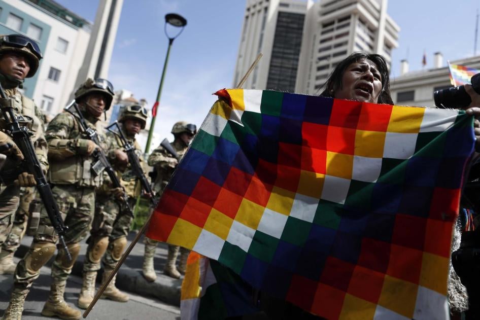 A demonstrator holds a Wiphala flag in front of soldiers blocking a street in downtown La Paz, Bolivia, Friday, Nov. 15, 2019.