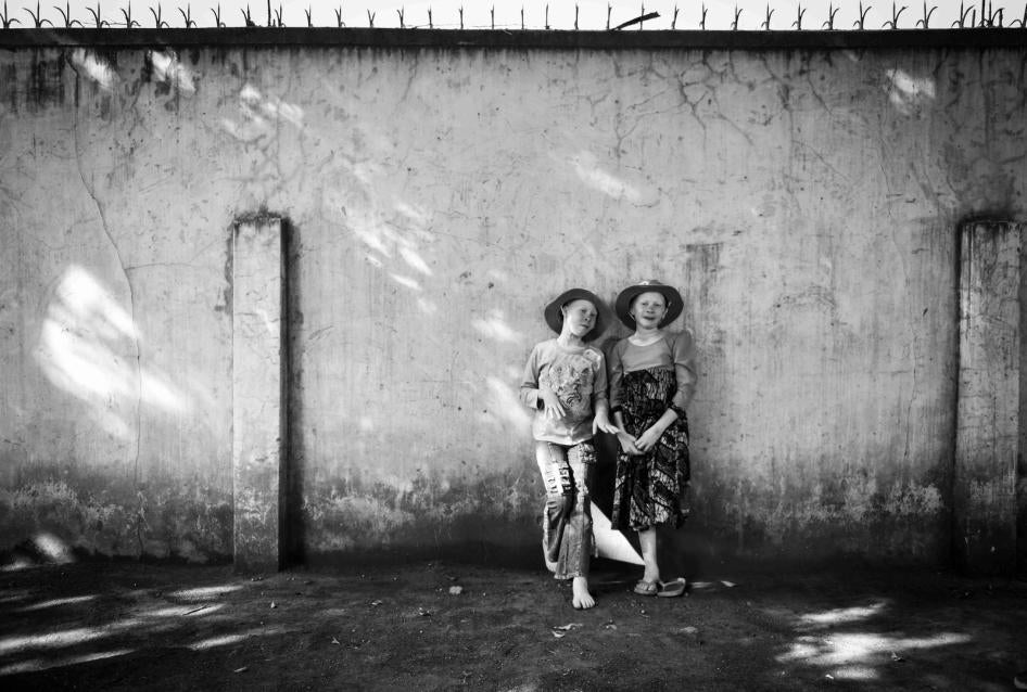 Two girls with albinism stand next to a wall 