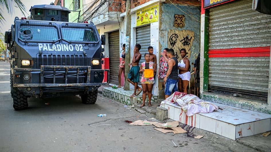 Um veículo blindado da polícia militar passa ao lado de uma pessoa morta pela polícia, em 7 de abril de 2016, na favela do Jacarezinho. A polícia militar matou outras duas pessoas nessa mesma operação.