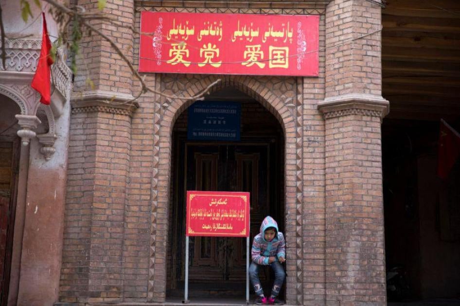 A child rests near the entrance to a mosque, where a banner reads "Love the party, Love the country" in the old city district of Kashgar in western China's Xinjiang region, November 4, 2017. © 2017 AP Photo/Ng Han Guan