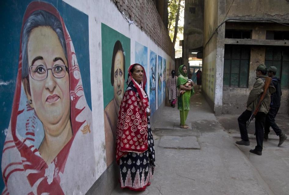 A Bangladeshi woman stands next to a mural displaying a portrait of Bangladesh Prime Minister Sheikh Hasina, left, Dhaka, Bangladesh on December 30, 2018.