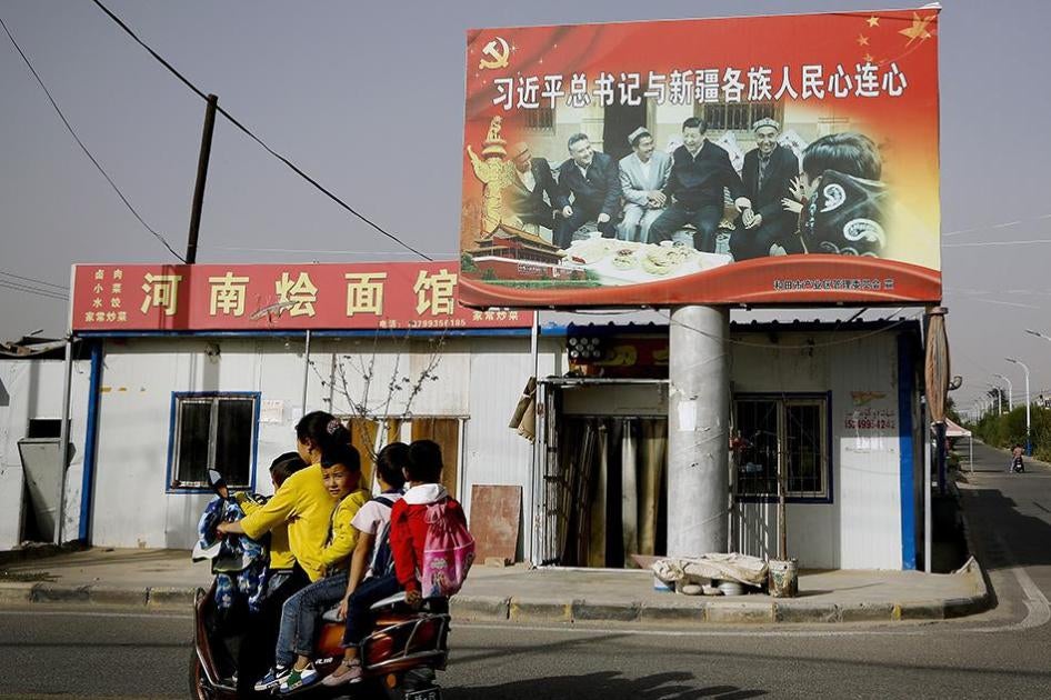 A Uighur woman picking up school children rides past a picture showing China's President Xi Jinping joining hands with a group of Uighur elders at the Unity New Village in Hotan, in western China's Xinjiang region. 