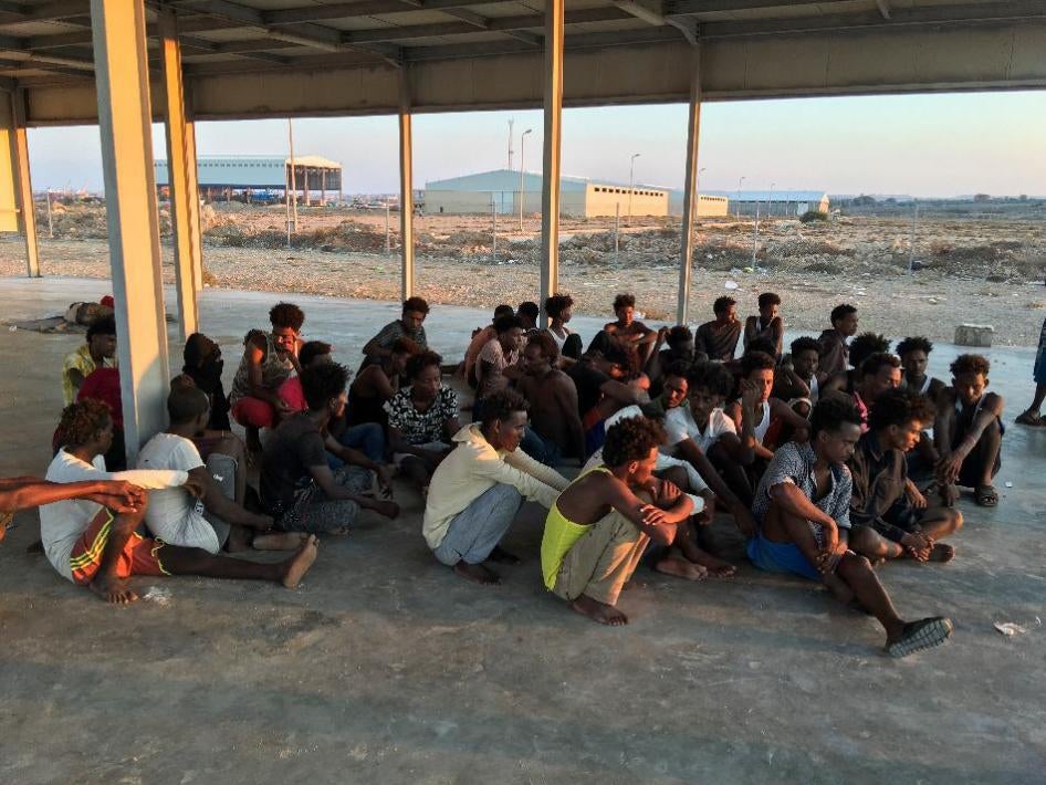 Des migrants secourus sont assis sur une côte à quelque 100 kilomètres à l'est de Tripoli, en Libye,