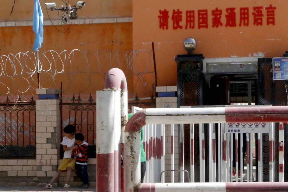 Children play outside the entrance to a school ringed with barbed wire, security cameras, and barricades, in Peyzawat, Xinjiang, August 31, 2018.