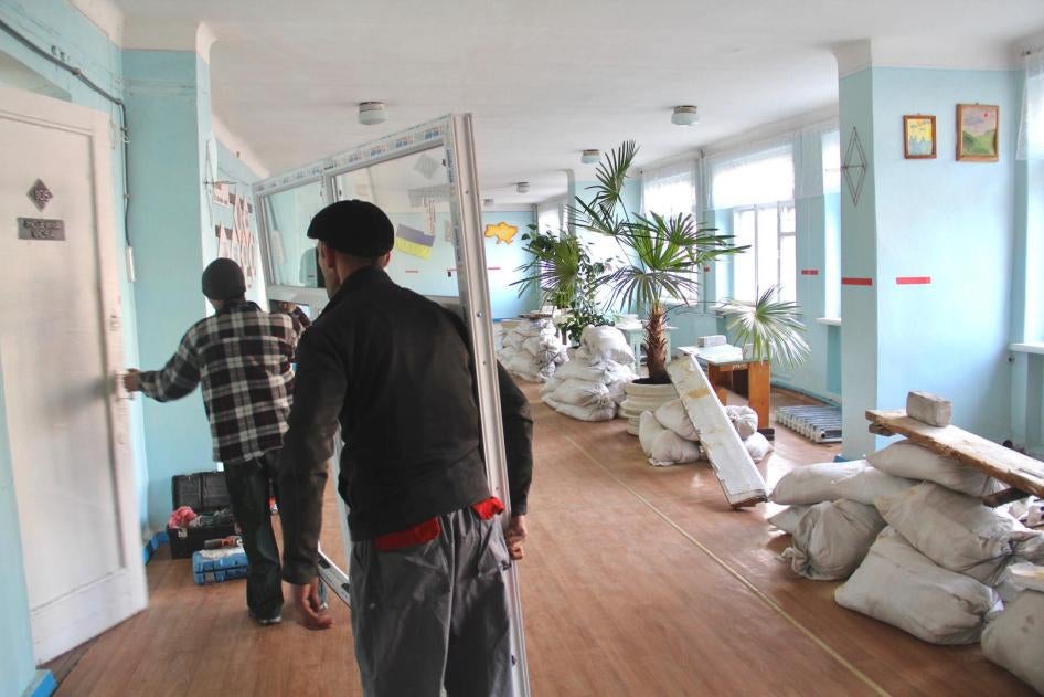 Two men carry replacement windows through a school in eastern Ukraine. The old windows were blown out when the school was hit by an explosive weapon