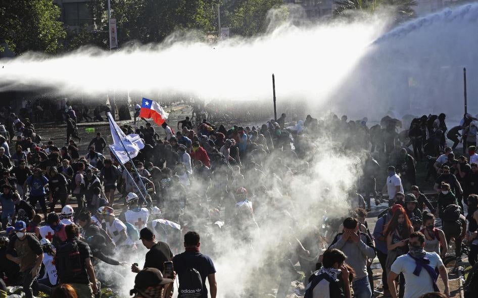 Des manifestants fuient sous des nuages de fumée blanche causés par des gaz lacrymogènes tirés par la police, qui a également recouru à des canons à eau afin de disperser ce grand rassemblement tenu à Santiago, au Chili, le dimanche 20 octobre 2019.