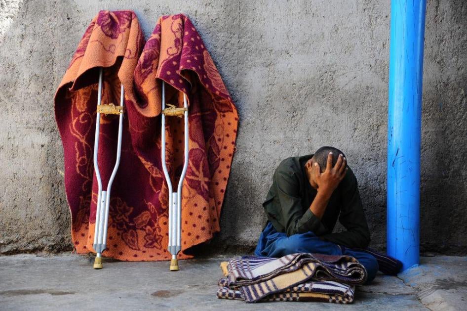 Recouvrant son visage, un homme est assis devant un mur contre lequel sont posées ses béquilles, dans la cour d'un établissement de soins de santé mentale à Herat, en Afghanistan, en avril 2014.
