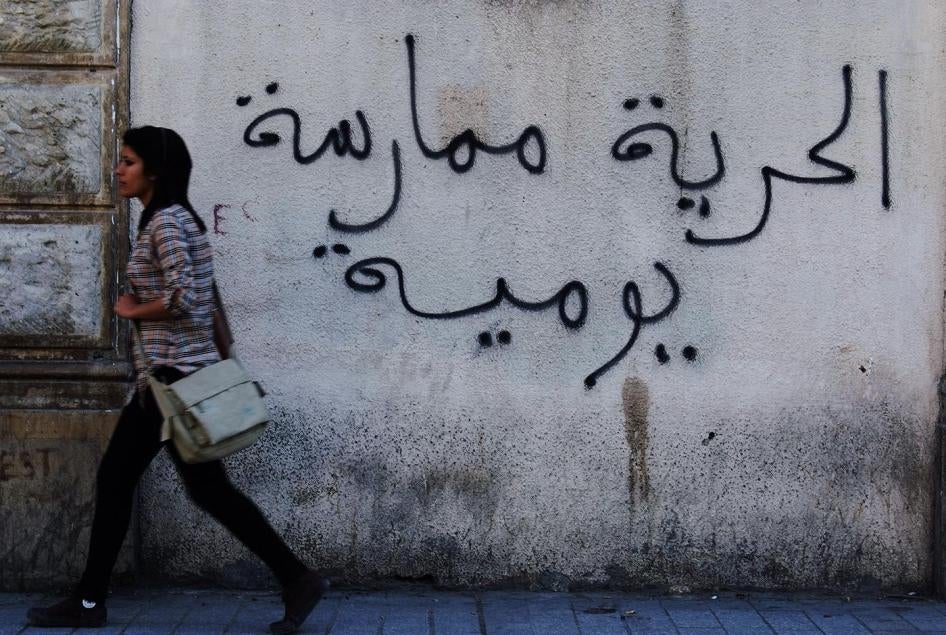امرأة تونسية تسير أمام جدار كُتِبت عليه عبارة "الحرية ممارسة يومية" في العاصمة تونس، 26 أبريل/نيسان 2011. 