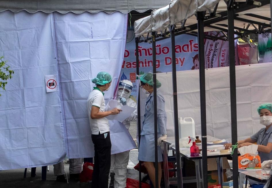 A man in a Hazmat suite talks with a nurse at a makeshift screening facility outside Rajadamnern boxing stadium in Bangkok, Thailand, March 19, 2020.