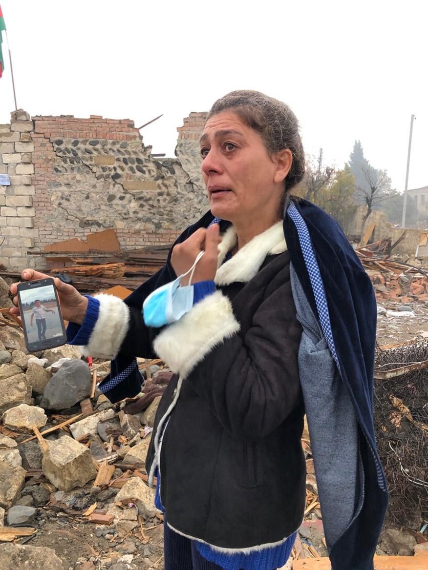 47-летняя Шаира Гулиева на фоне развалин своего дома с фотографией 13-летнего племянника Артура Гулиева, умершего от ран через неделю после попадания оперативно-тактической ракеты 17 октября 2020 г. 