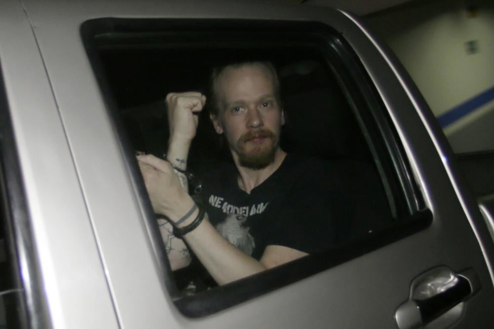 A man holds up his handcuffed wrists from the inside of a car