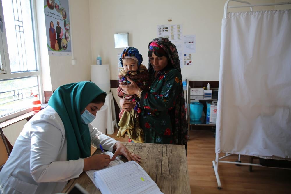 A healthcare worker fills out a form while a woman and her baby look on