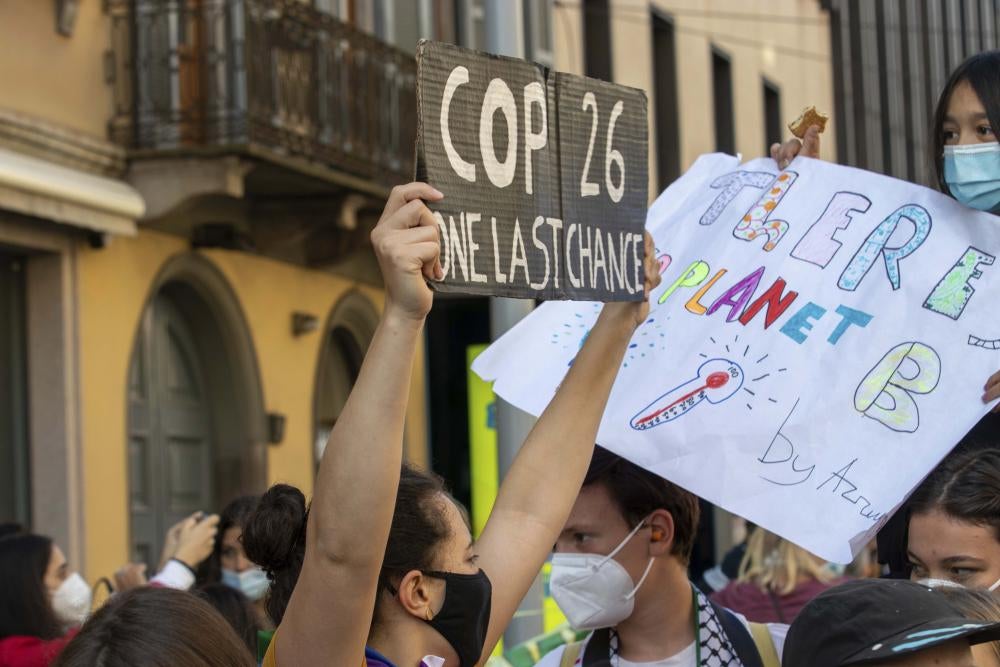 A masked person holds a sign that says "COP26: One Last Chance"