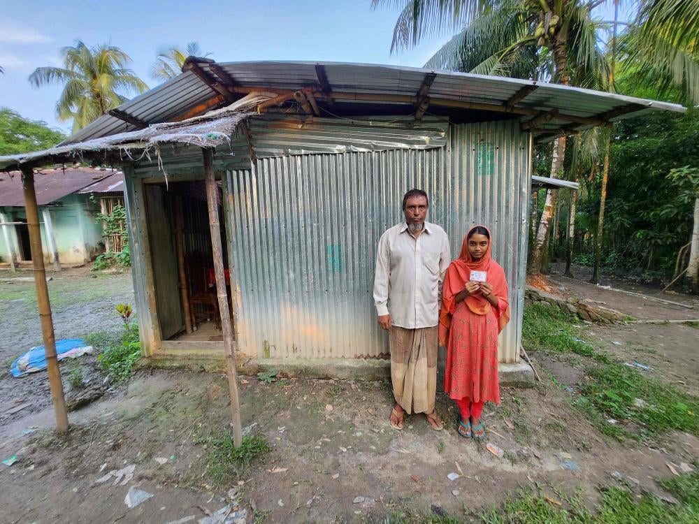Nilima Islam, une jeune fille de 15 ans avec un handicap auditif et d'élocution, avec son père, Nurul Islam, devant leur maison à Bishwanath (district de Sylhet) au Bangladesh. Lors des inondations de juin 2022, ils se sont réfugiés chez un voisin. Le père de Nilima a dit qu'elle était terrifiée en voyant la montée des eaux. 