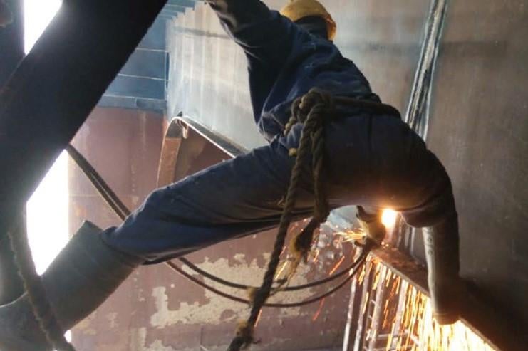 A shipbreaking worker balances on the ledge of a ship to torch through the steel.