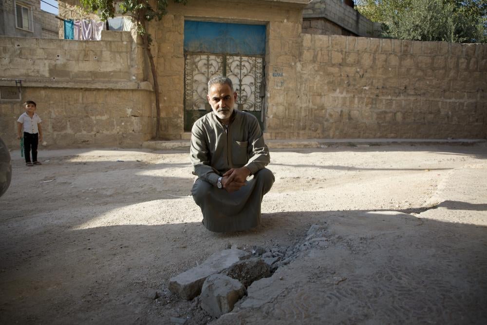 Taha Amouri kneels beside the spot where one of the submunition from the cluster munitions attack on the town of Termanin landed, injuring his brother on October 6 and later claiming his life.